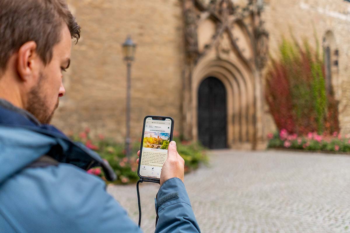 Ein Mann schaut auf sein Smartphone auf dem die Webapp 'Der Kreis von Goseck' zu sehen ist.